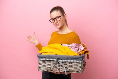Pembe arka planda izole edilmiş çamaşır sepeti tutan beyaz bir kadın davet edildiği için ellerini yana uzatıyor.