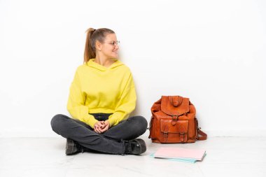 Beyaz arka planda beyaz bir zeminde oturan beyaz tenli genç bir kadın.