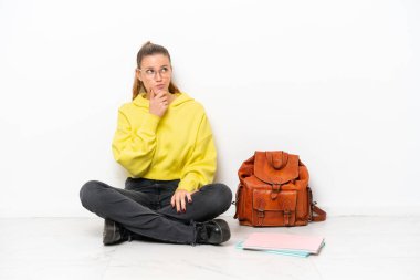 Beyaz arka planda beyaz bir zeminde oturan genç beyaz bir kadın şüpheleri vardı ve kafası karışmıştı.