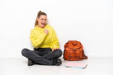Young student caucasian woman sitting one the floor isolated on white background celebrating a victory