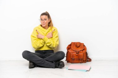 Beyaz arka planda beyaz bir zeminde oturan beyaz tenli genç bir kadın, yan taraftakilerin şüphelerine işaret ediyor.