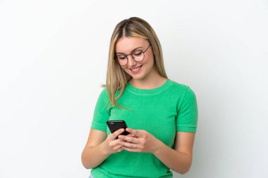 Beyaz arka planda izole edilmiş genç beyaz kadın cep telefonuyla mesaj gönderiyor.