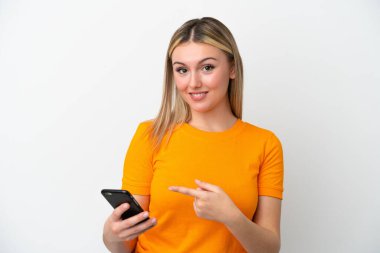 Young caucasian woman isolated on white background using mobile phone and pointing it