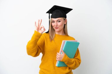 Beyaz arka planda izole edilmiş beyaz tenli genç bir kadın parmaklarıyla tamam işareti gösteriyor.