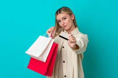 Mavi arka planda izole edilmiş beyaz bir kadın elinde alışveriş çantaları ve bir kredi kartı tutuyor.