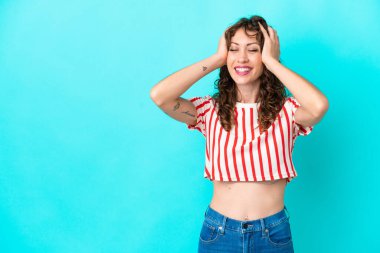 Kıvırcık saçlı genç bir kadın mavi arka planda yalnız gülüyor.