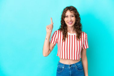 Mavi arka planda izole edilmiş kıvırcık saçlı genç kadın harika bir fikre işaret ediyor.