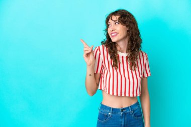 Mavi arka planda izole edilmiş kıvırcık saçlı genç bir kadın parmağını kaldırarak çözümü bulmaya çalışıyor.