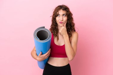 Genç sporcu kadın yoga derslerine gidiyor pembe arka planda bir minder tutarken kuşkuları ve düşünceleri var.