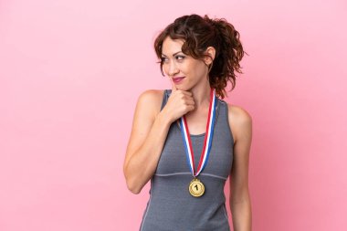 Pembe arka planda madalyaları olan genç beyaz kadın yan tarafa bakıyor.
