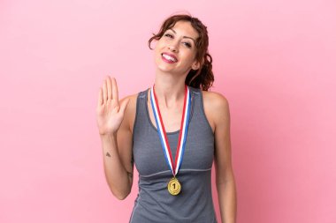 Pembe arka planda madalyalı beyaz bir kadın. Mutlu bir ifadeyle selamlıyor.