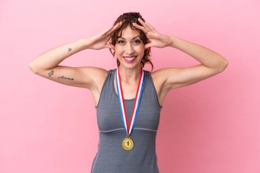 Pembe arka planda, sürpriz bir ifadeyle madalyalı beyaz bir kadın.