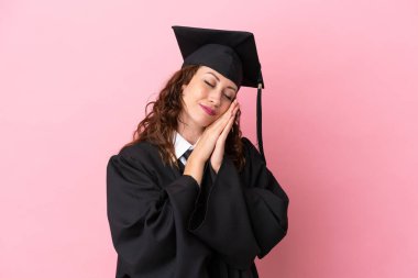 Üniversiteden mezun genç bir kadın pembe arka planda izole edilmiş bir şekilde uyku jesti yapıyor.