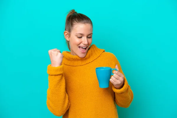 Young caucasian woman holding cup isolated on blue background celebrating a victory