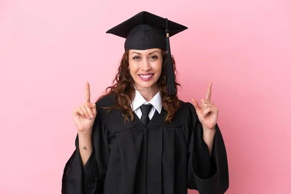 Young university graduate woman isolated on pink background pointing up a great idea