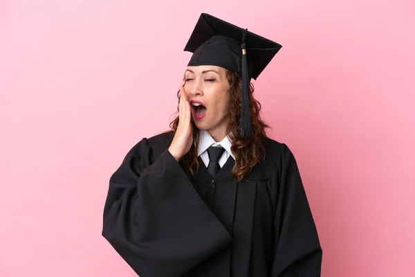 Young university graduate woman isolated on pink background yawning and covering wide open mouth with hand