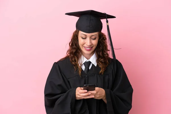 Young university graduate woman isolated on pink background sending a message with the mobile