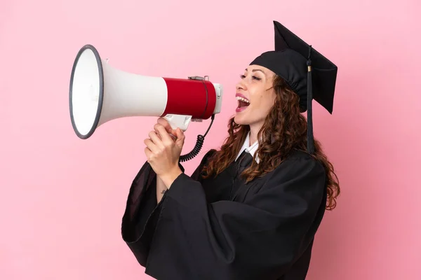 Young university graduate woman isolated on pink background shouting through a megaphone