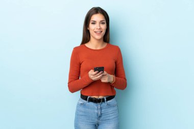 Mavi arka planda izole genç beyaz kadın şaşırdı ve bir mesaj gönderiyor.