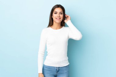 Mavi arka planda izole edilmiş genç beyaz kadın gülüyor.