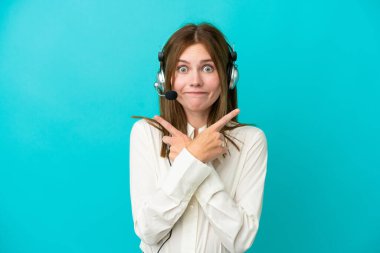 Tele pazarlamacı İngiliz kadın mavi arka planda izole edilmiş bir kulaklıkla çalışıyor.