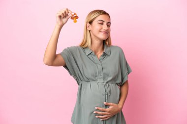 Genç Uruguaylı kadın mavi arka planda izole edilmiş hamile ve emzik taşıyor.