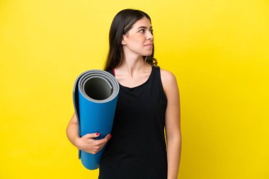 İtalyan spor kadını yoga derslerine gidiyor. Sarı arka planda tek başına. Yan tarafa bakıyor.