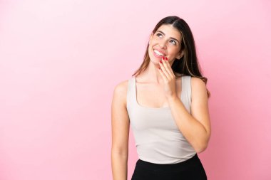 Genç İtalyan kadın pembe arka planda izole edilmiş gülümserken yukarı bakıyor