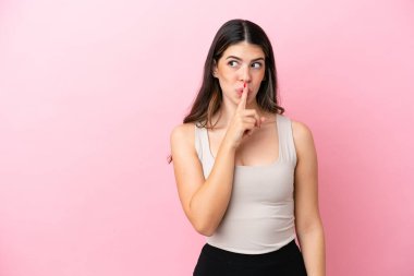 Pembe arka planda izole edilmiş genç bir İtalyan kadın sessizlik işareti gösteriyor. Parmağını ağzına sokuyor.