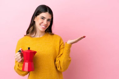 Pembe arka planda izole edilmiş kahve makinesini tutan genç İtalyan kadın davet etmek için ellerini yana uzatıyor.