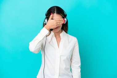 Tele pazarlamacı İtalyan kadın kulaklıkla çalışıyor mavi arka planda, gözleri elleriyle kapatan bir kulaklıkla. Bir şey görmek istemiyorum.