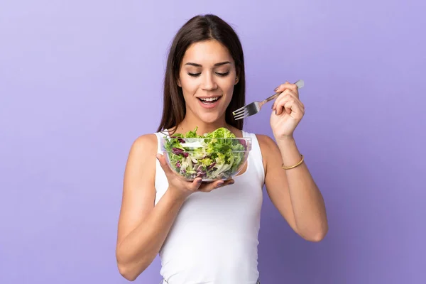 Young caucasian woman with salad isolated on purple background