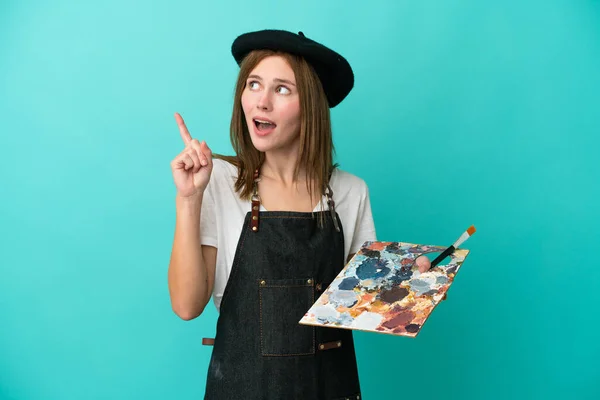 青い背景に孤立したパレットを持つ若いアーティストの英語の女性は 指を指差すアイデアを考えて — ストック写真