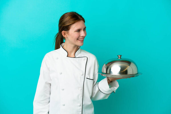 Young chef woman with tray isolated on blue background looking to the side and smiling