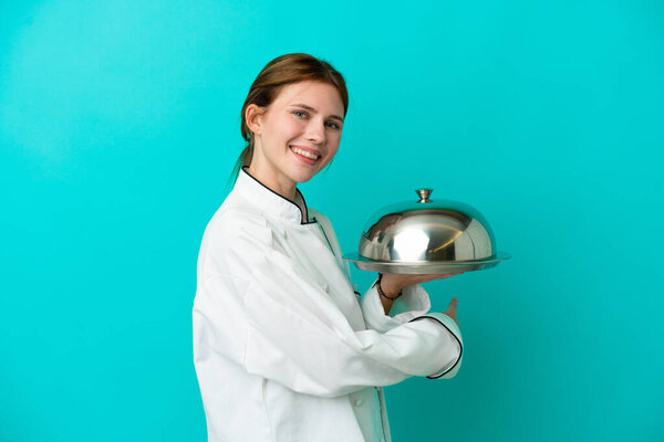 Young chef woman with tray isolated on blue background pointing back