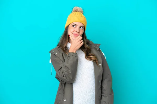 冬のジャケットと帽子を身に着けている若いイタリア人女性は疑問を持ち 顔の表情を混乱させる青い背景に隔離されています — ストック写真