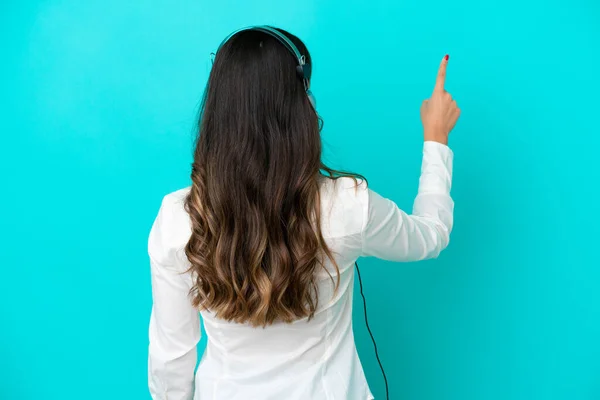 テレマーケティングイタリアの女性は インデックスの指で後ろを指して青い背景に隔離されたヘッドセットで作業しています — ストック写真