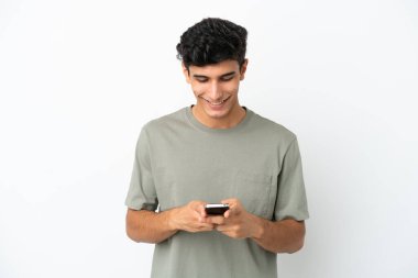 Beyaz arka planda izole edilmiş genç Arjantinli adam cep telefonuyla mesaj gönderiyor.