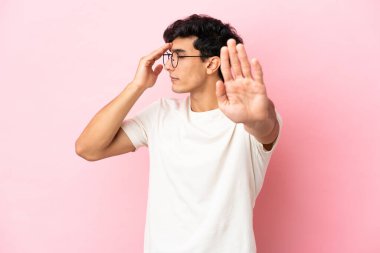 Pembe arka planda izole edilmiş genç Arjantinli adam jesti durdurup yüzünü kapatıyor.