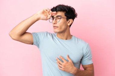 Arjantinli genç bir adam pembe arka planda gözlüklü ve yorgun