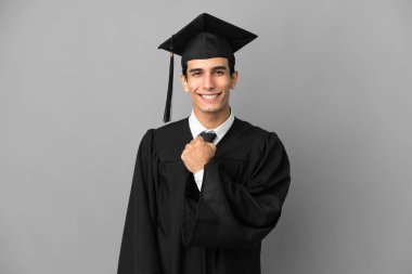 Genç Arjantinli üniversite mezunu. Gri arka planda izole bir şekilde zaferi kutluyor.