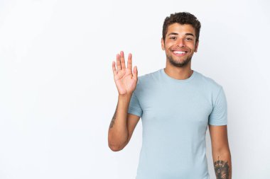 Genç yakışıklı Brezilyalı adam beyaz arka planda izole edilmiş mutlu bir ifadeyle selamlıyor.