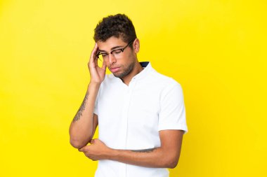 Genç ve yakışıklı Brezilyalı adam sarı arka planda izole edilmiş, baş ağrısı var.