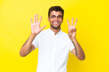 Sarı arka planda izole edilmiş yakışıklı Brezilyalı genç sekiz parmaklı sayıyor.