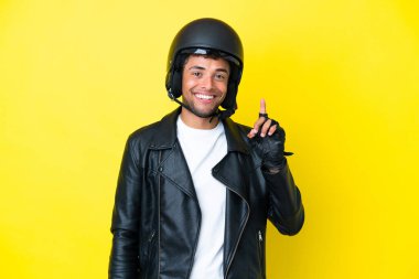 Sarı arka planda izole edilmiş motosiklet kasklı genç Brezilyalı adam harika bir fikre işaret ediyor.