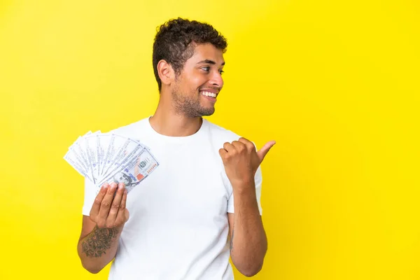 Jonge Braziliaanse Man Neemt Veel Geld Geïsoleerd Gele Achtergrond Wijzend — Stockfoto