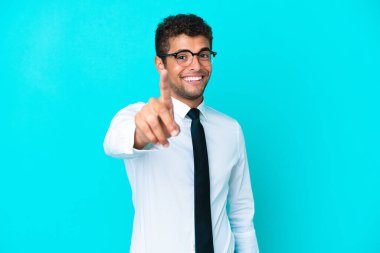 Genç Brezilyalı iş adamı mavi arka planda izole edilmiş ve parmağını kaldırıyor.