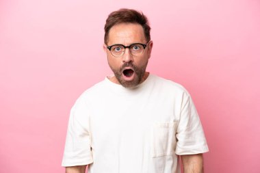 Orta yaşlı beyaz bir adam pembe arka planda izole edilmiş gözlüklü ve şaşırmış bir ifadeyle