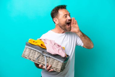 Mavi arka planda izole edilmiş çamaşır sepeti tutan orta yaşlı bir kadın ağzı sonuna kadar açık bağırıyor.