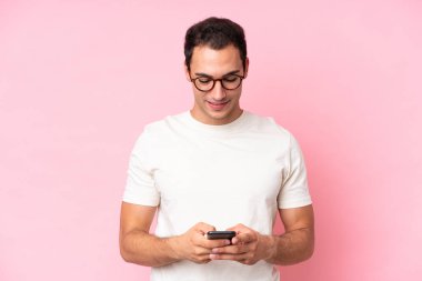 Pembe arka planda izole edilmiş genç beyaz adam cep telefonuyla bir mesaj gönderiyor.